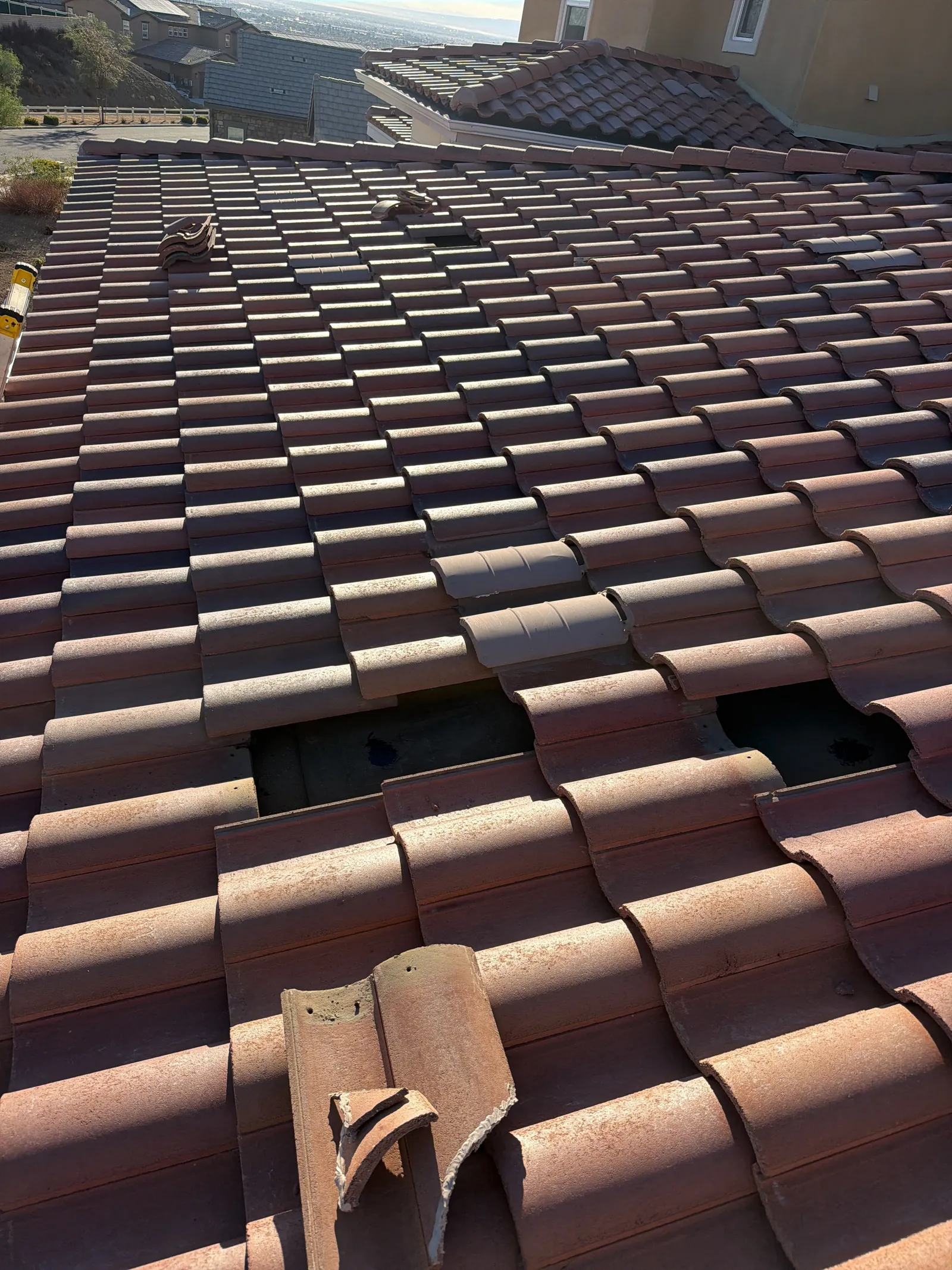 Clay S-tile roof opened up for repair, with broken tile pieces and the underlayment showing
