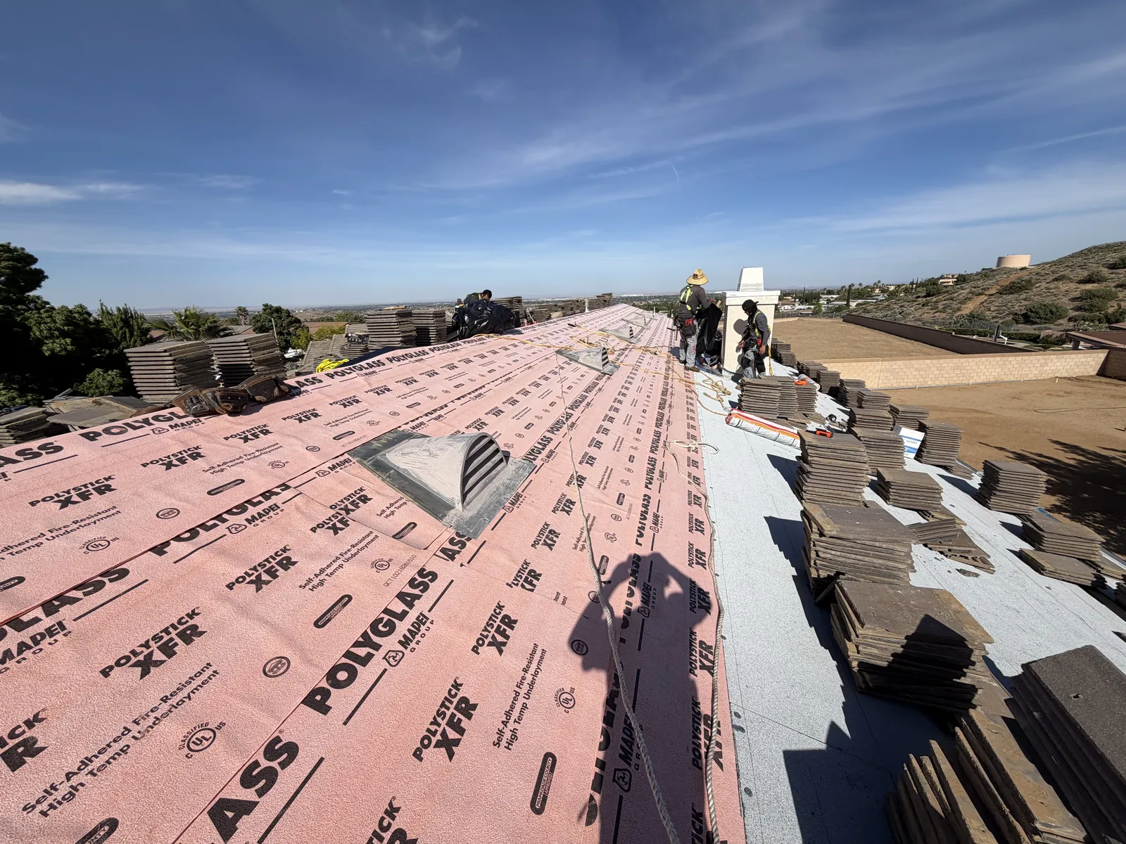 Pink Polyglass self-adhered underlayment rolled out across a roof, with tile stacked beside it